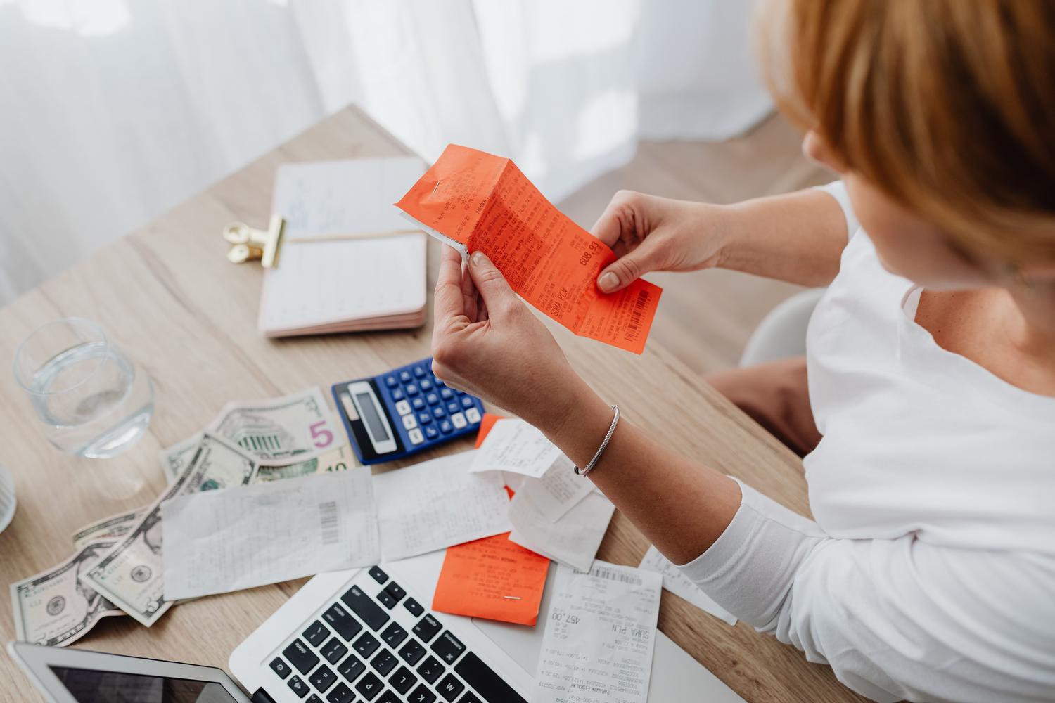 Persona utilizando una calculadora y recibos para gestionar los gastos eléctricos en su oficina en casa Persona utilizando una calculadora y recibos para gestionar los gastos eléctricos en su oficina en casa