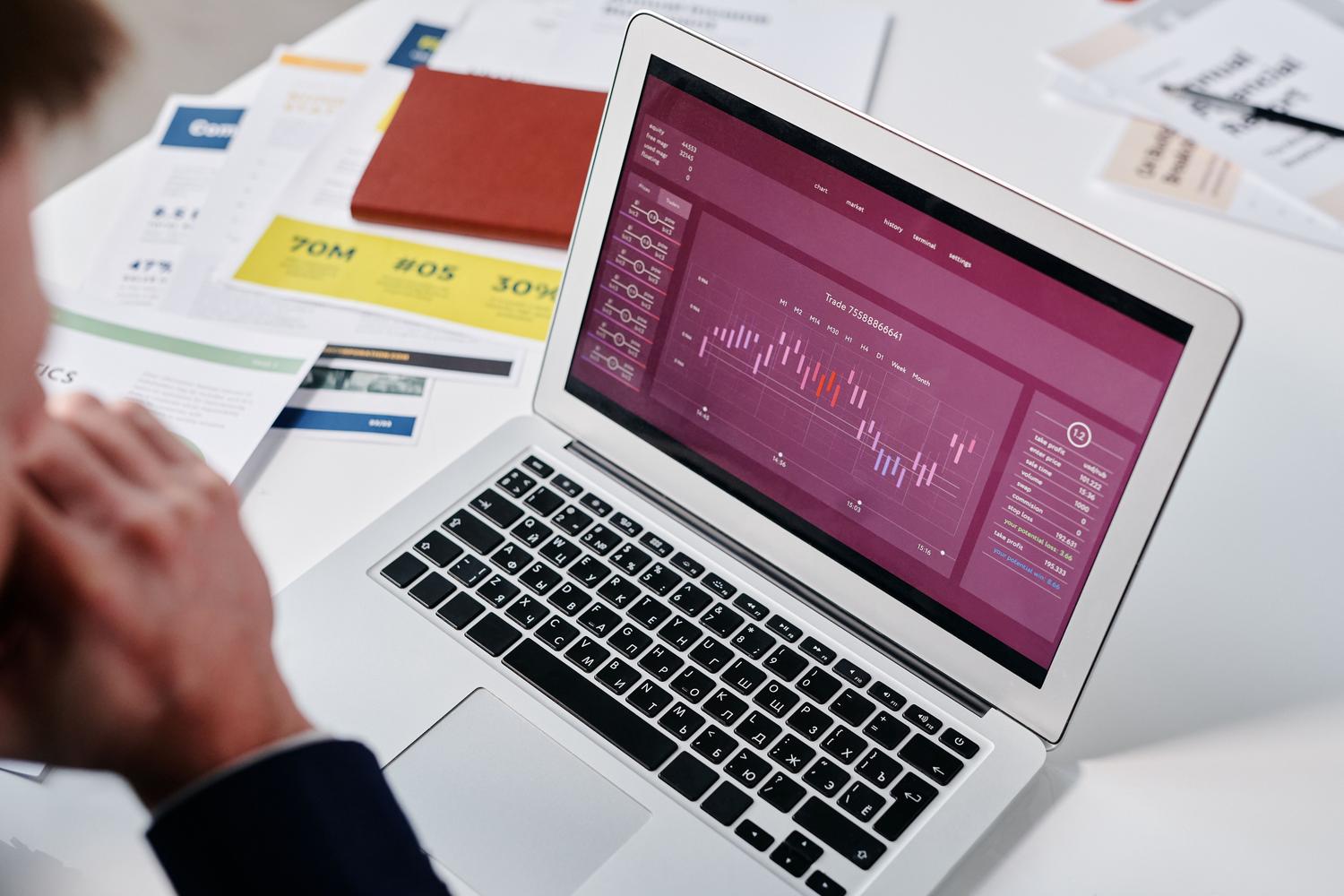 Profesional analizando un dashboard de datos inteligente en un portátil con reportes físicos al lado. Profesional analizando un dashboard de datos inteligente en un portátil con reportes físicos al lado.