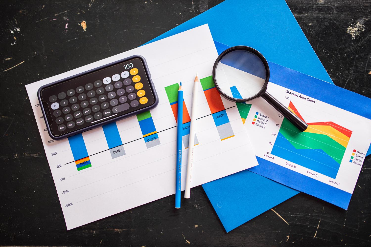 Vista superior de gráficos financieros con una calculadora, lupa y lápices sobre un escritorio, representando el análisis de retorno de inversión (ROI) de la IA. Vista superior de gráficos financieros con una calculadora, lupa y lápices sobre un escritorio, representando el análisis de retorno de inversión (ROI) de la IA.