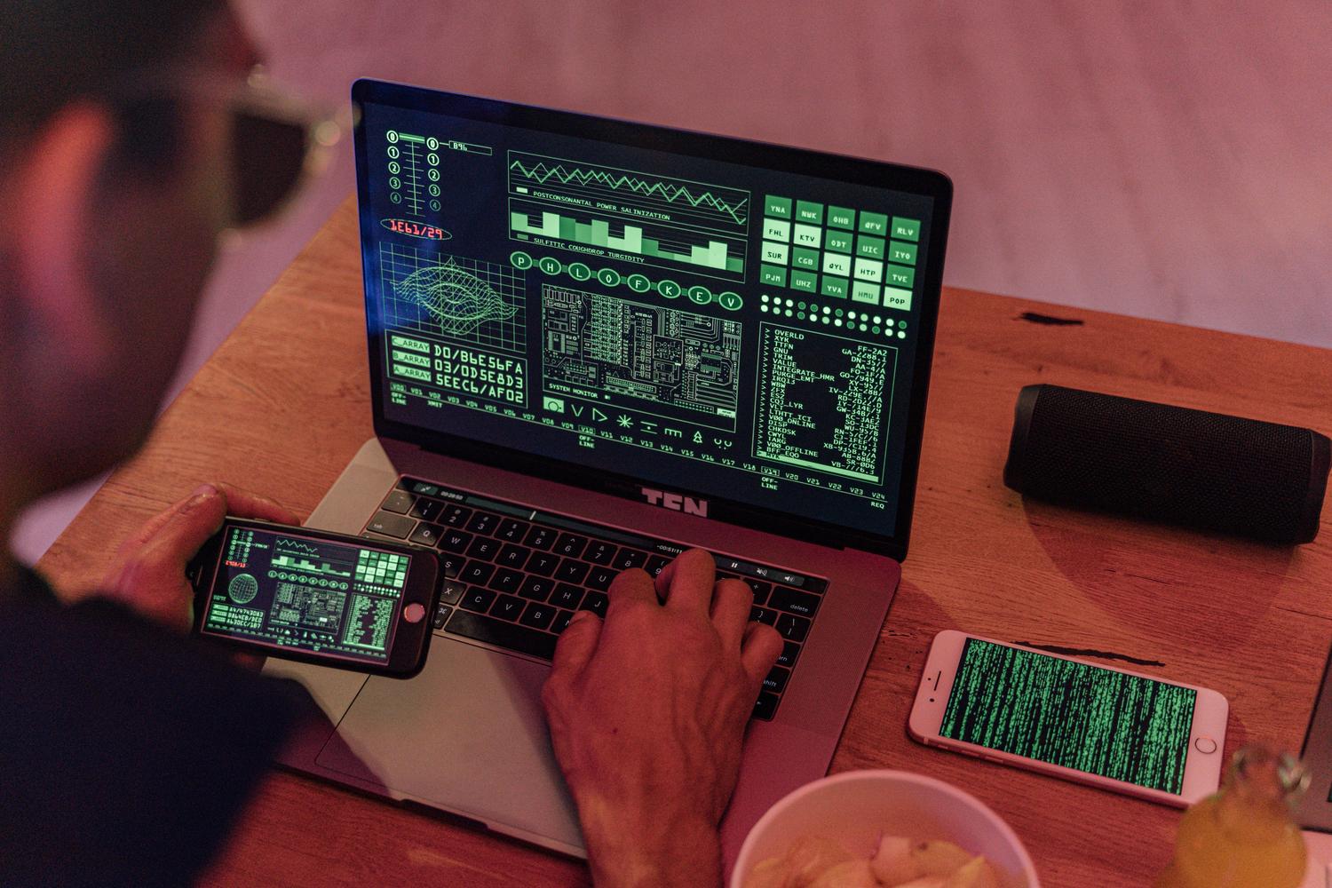 Persona utilizando herramientas de ciberseguridad en un portátil y móvil con pantallas de código verde, representando la parte técnica de la recuperación de cuentas. Persona utilizando herramientas de ciberseguridad en un portátil y móvil con pantallas de código verde, representando la parte técnica de la recuperación de cuentas.