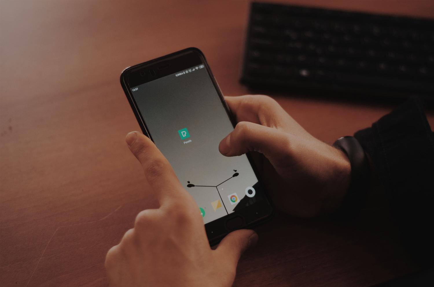 Manos operando un smartphone sobre un escritorio de madera junto a un teclado, representando productividad y gestión de chats. Manos operando un smartphone sobre un escritorio de madera junto a un teclado, representando productividad y gestión de chats.